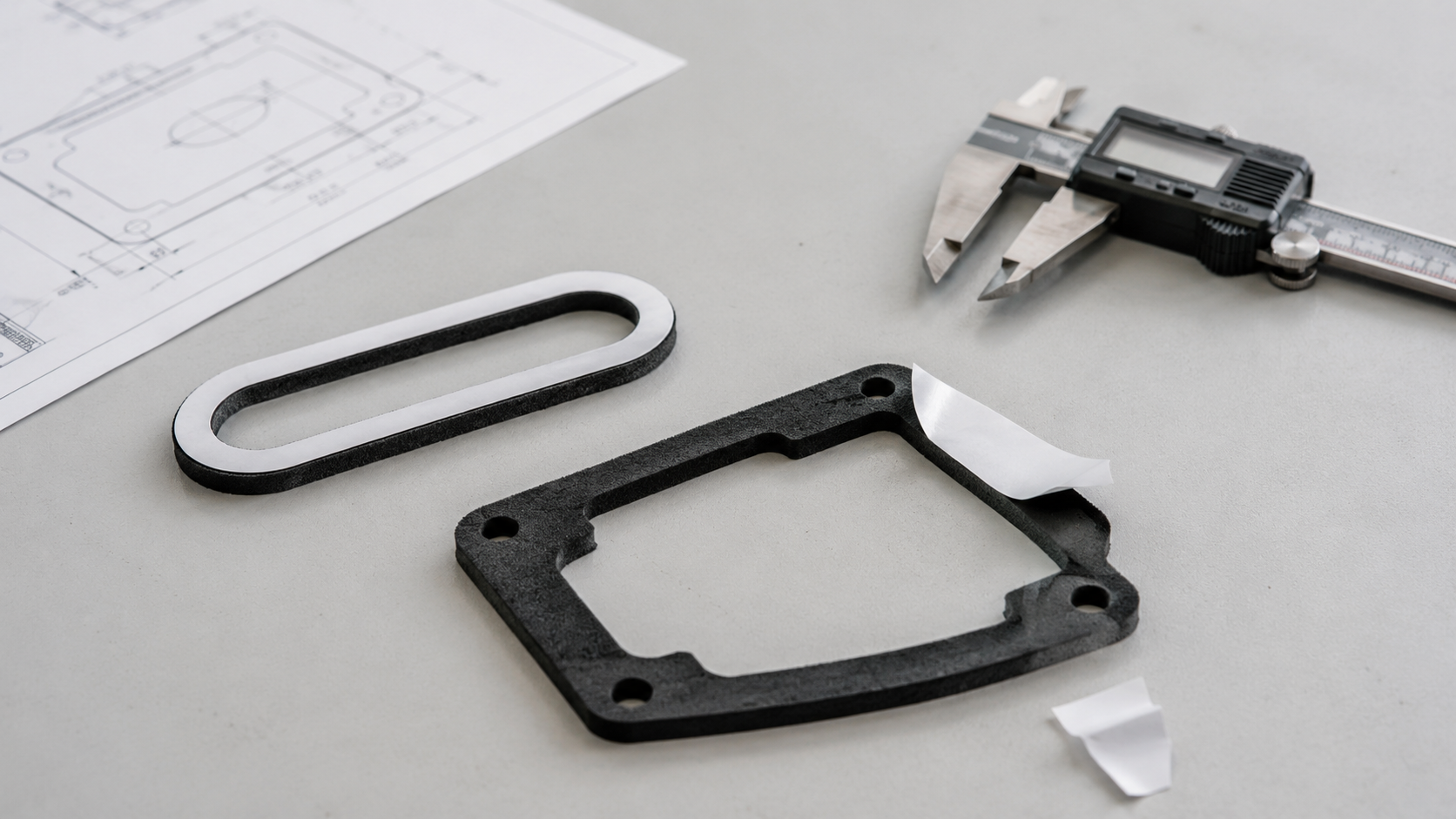 Professional OEM packaging and inspection scene showing custom adhesive foam gaskets supplied in sheets, rolls, and kits, including kiss-cut foam gaskets on release liner, adhesive foam frames, foam cushioning pads, pull-tab designs, clean trays, protective bags, calipers, thickness gauges, peel testing tools, and organized production batches