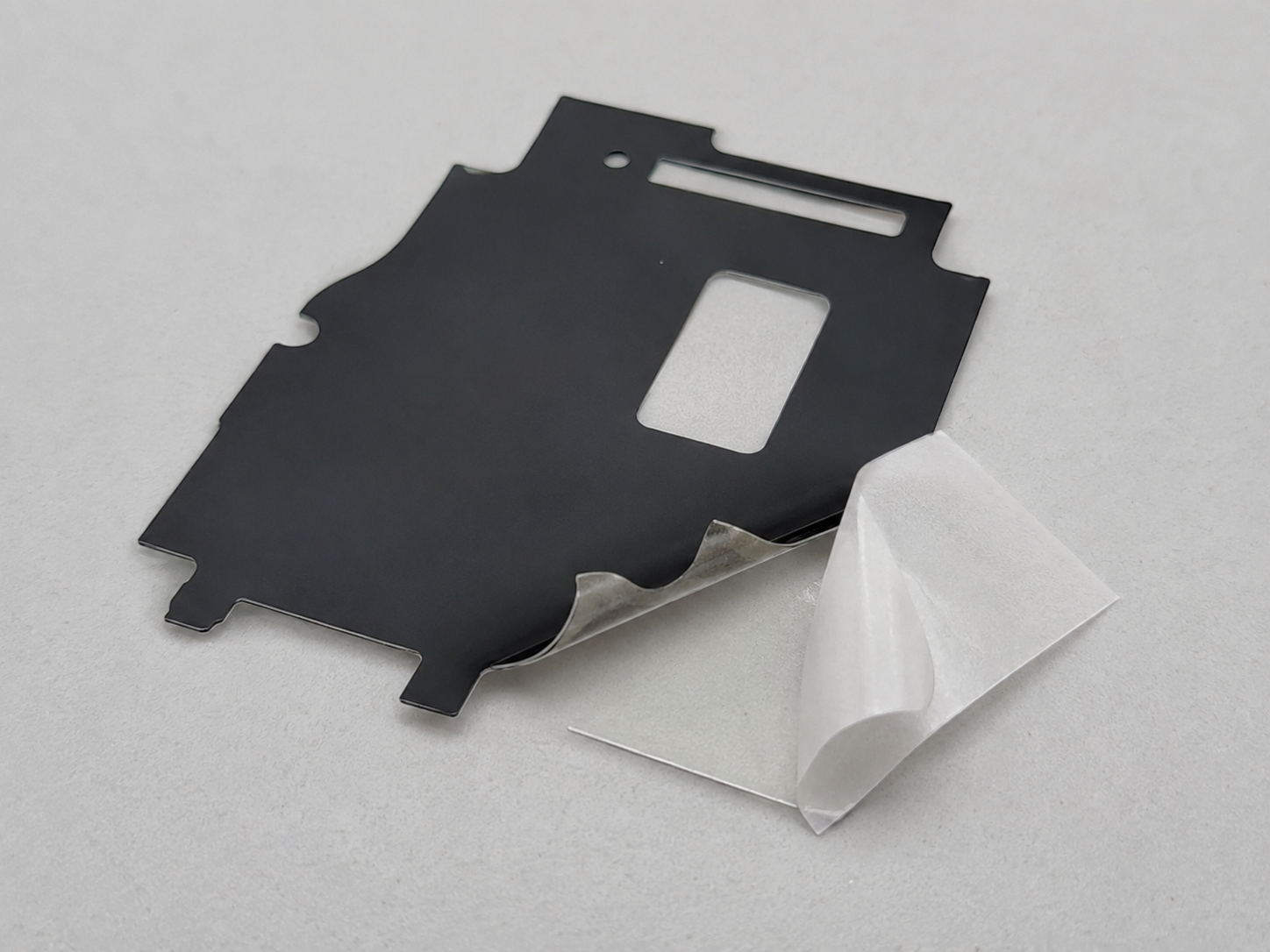 Image Description: Clean optical component development scene showing adhesive-backed black PET light-blocking films, die cut optical masks, release liners, inspection fixtures, magnification tools, and dimensional measurement equipment on an OEM engineering table. No complete displays, products with logos, readable text, labels, arrows, or icons. Image width: 1600–1920 px. Target file size: 100–200 KB.